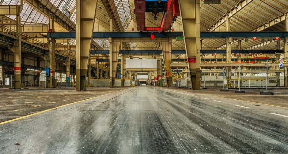 A wide empty industrial warehouse interior with overhead cranes