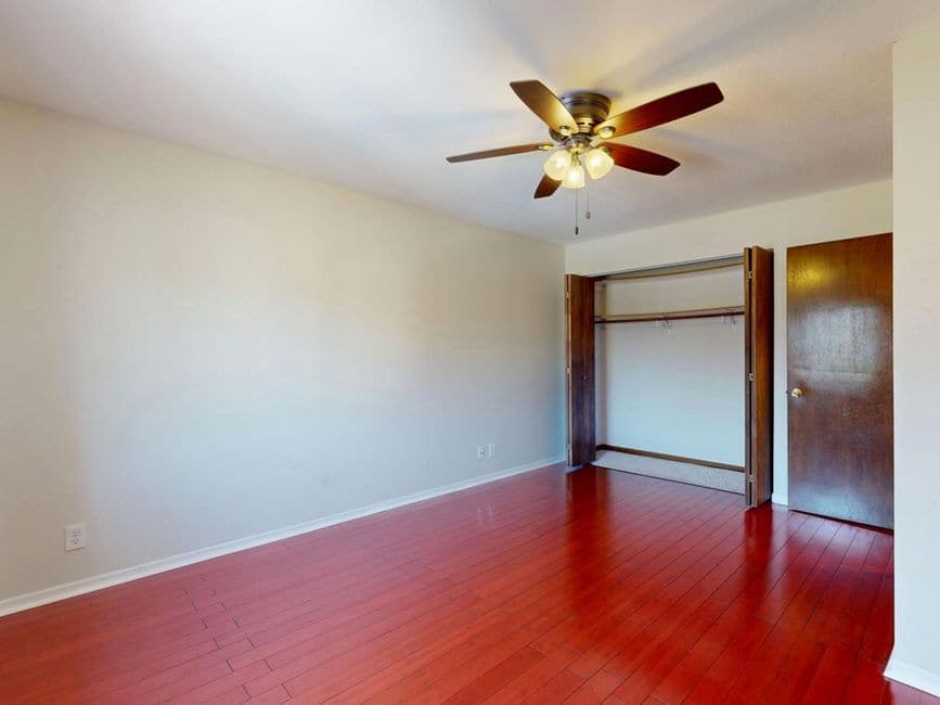 An empty room with hardwood floors and a ceiling fan