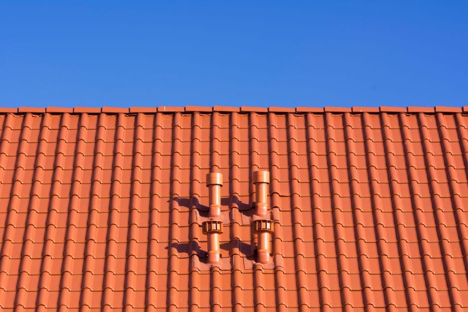 A red clay tile roof with vents under a clear sky