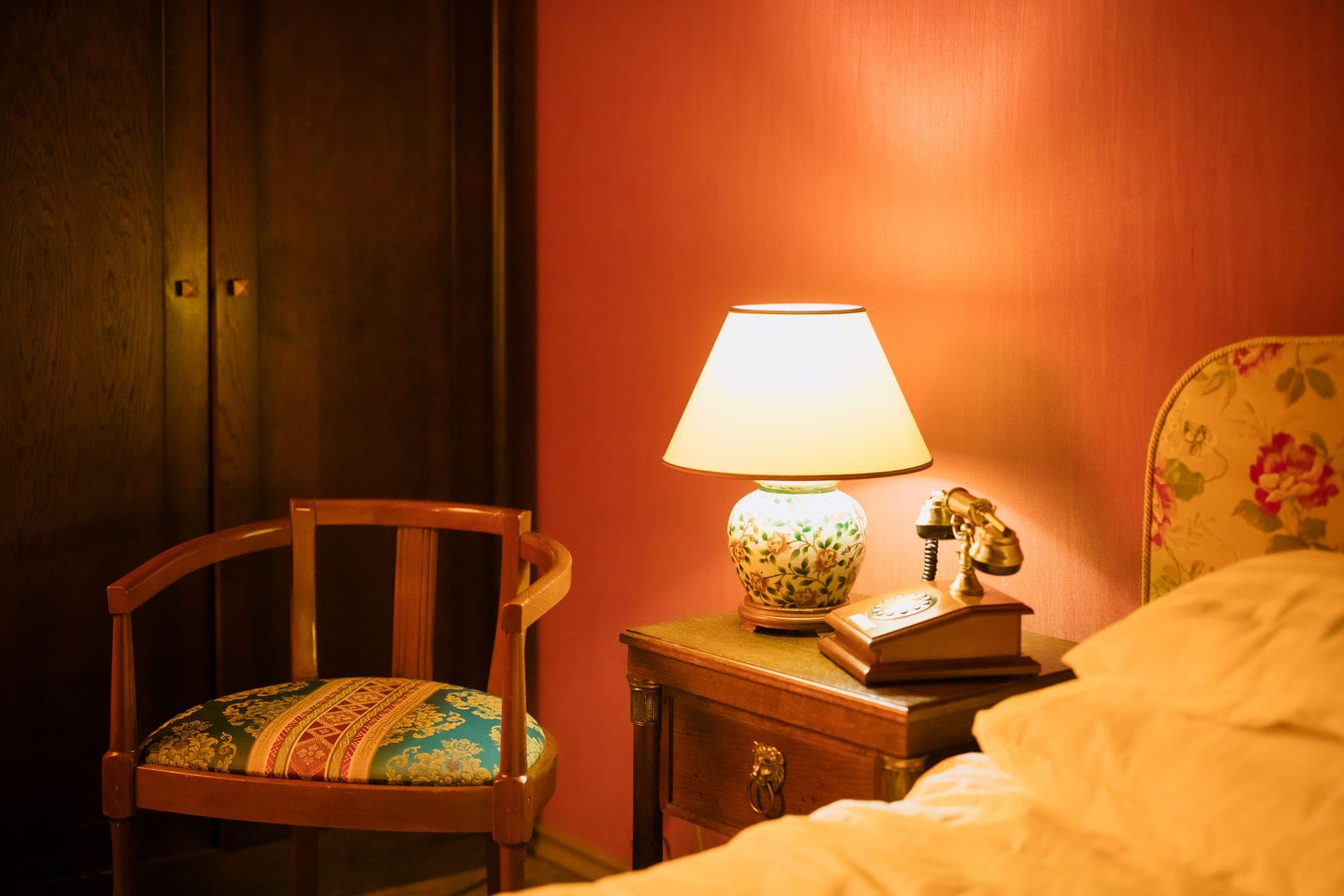 A dim bedroom with a bedside lamp and telephone