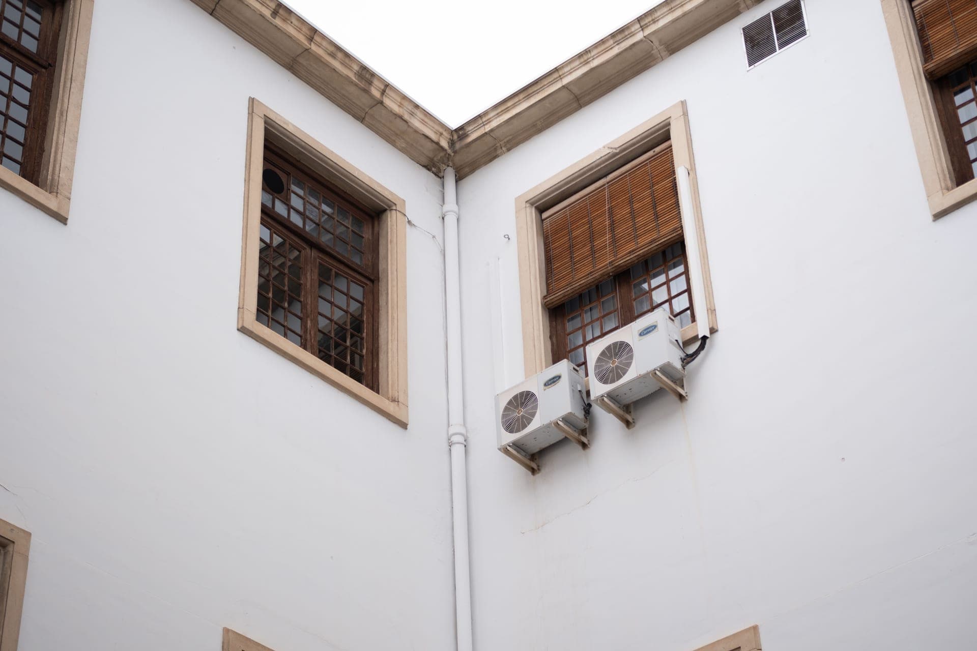 A building facade with rows of near-identical air conditioning units below wooden window shades