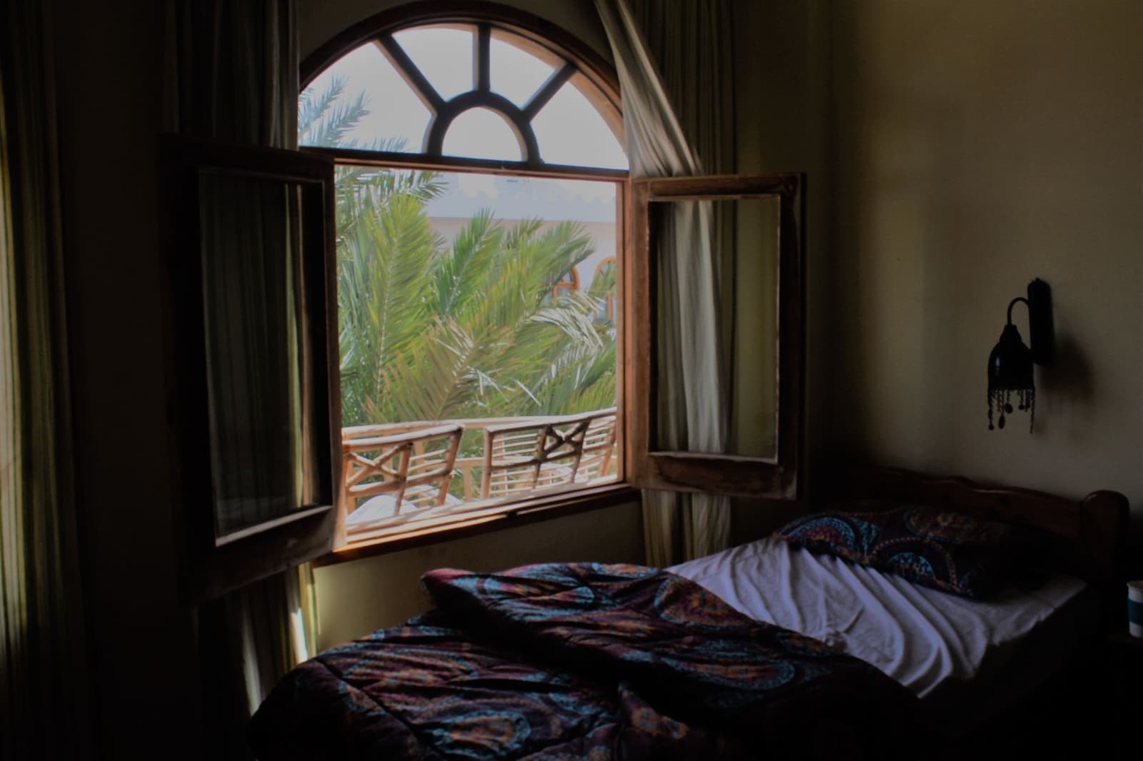 A bright bedroom with an open window and a view of palm trees