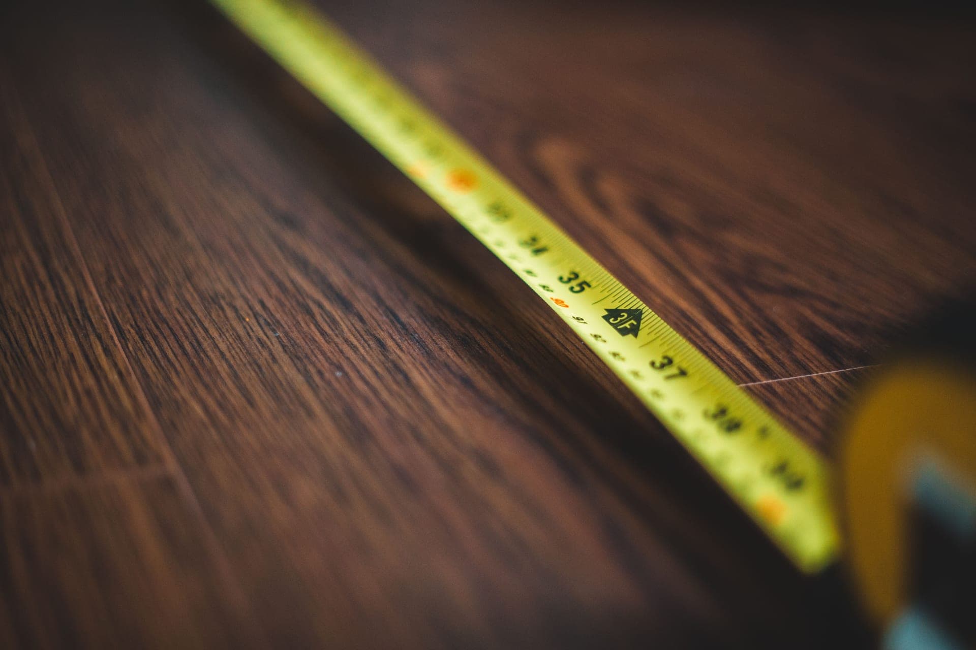 An empty room with bare wooden floorboards being measured in natural daylight