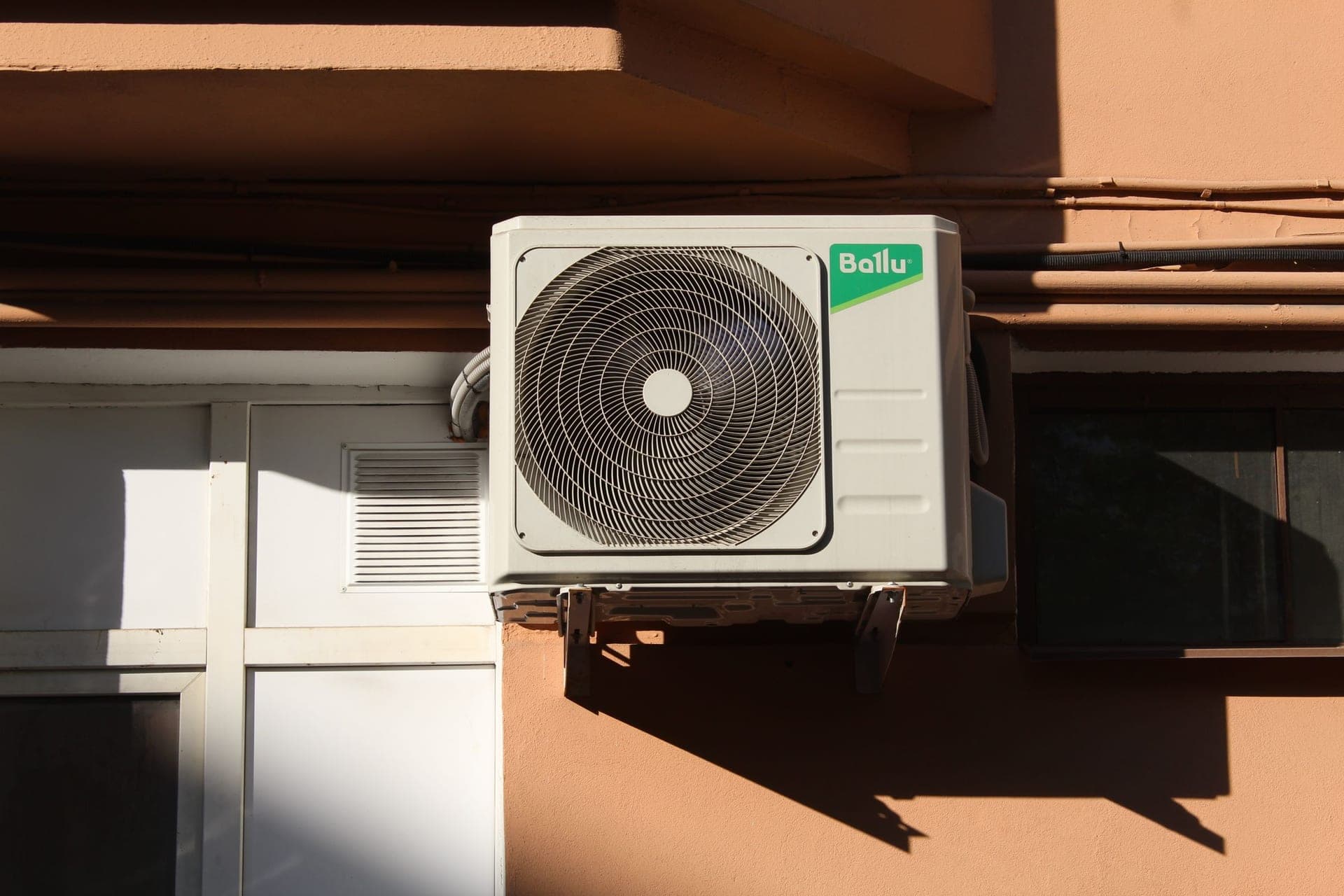 An air conditioning condenser unit mounted on an exterior wall in sunlight