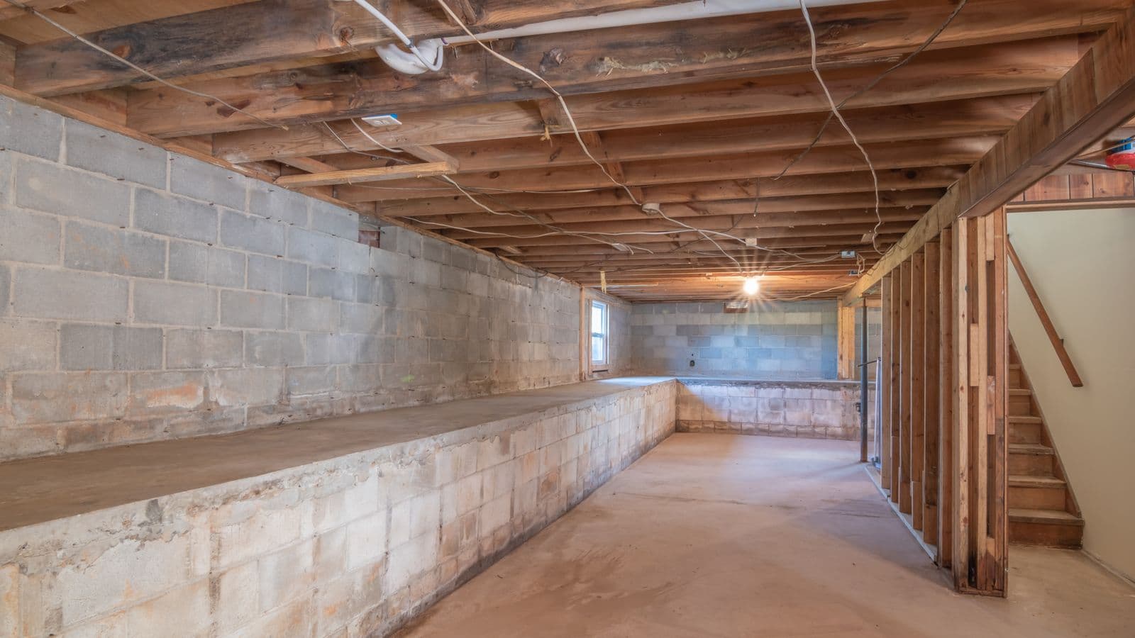 An empty basement with concrete walls, exposed beams and stairs