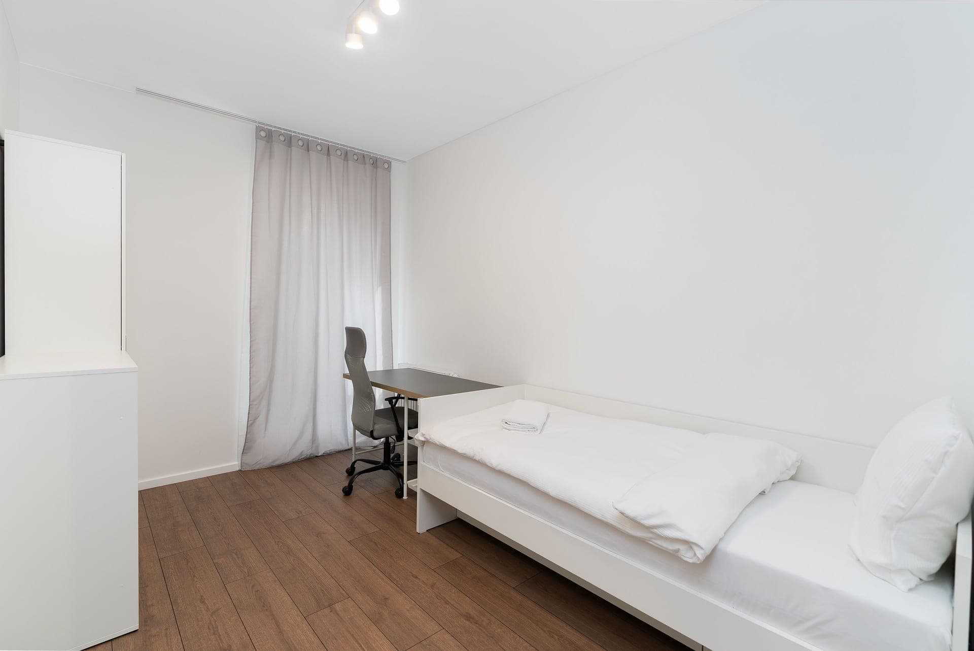 A small dorm room with a single bed and a desk under a window