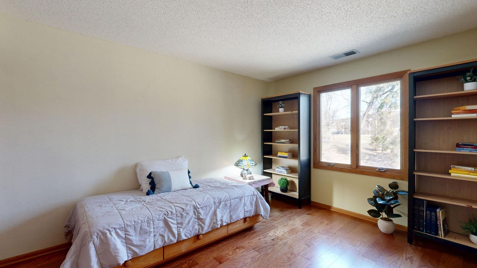 A bright minimalist bedroom with a made bed, bookshelves and a window