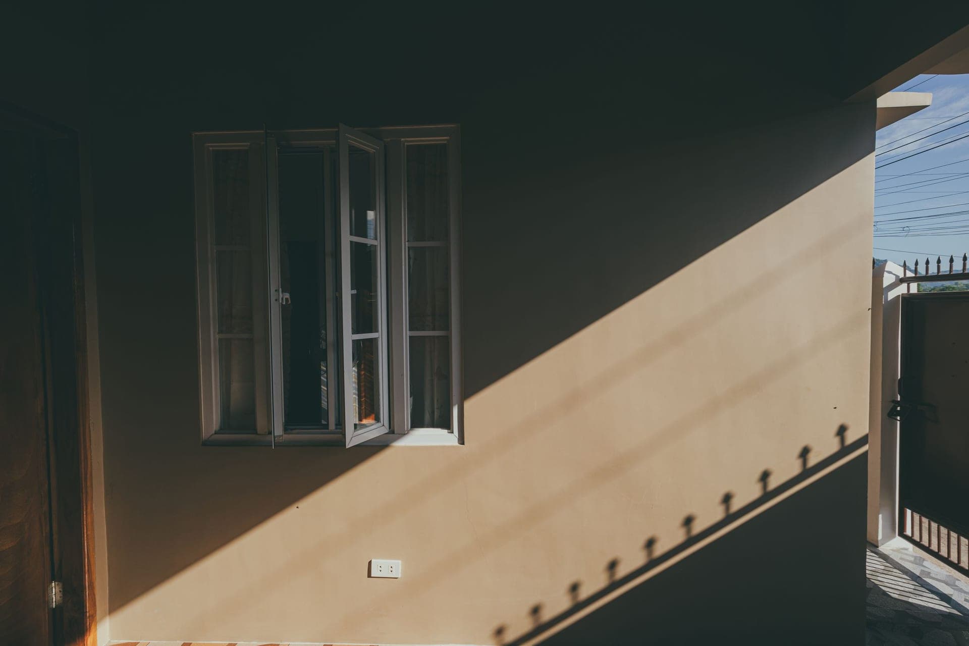An open window with hard afternoon sunlight falling across a plain wall