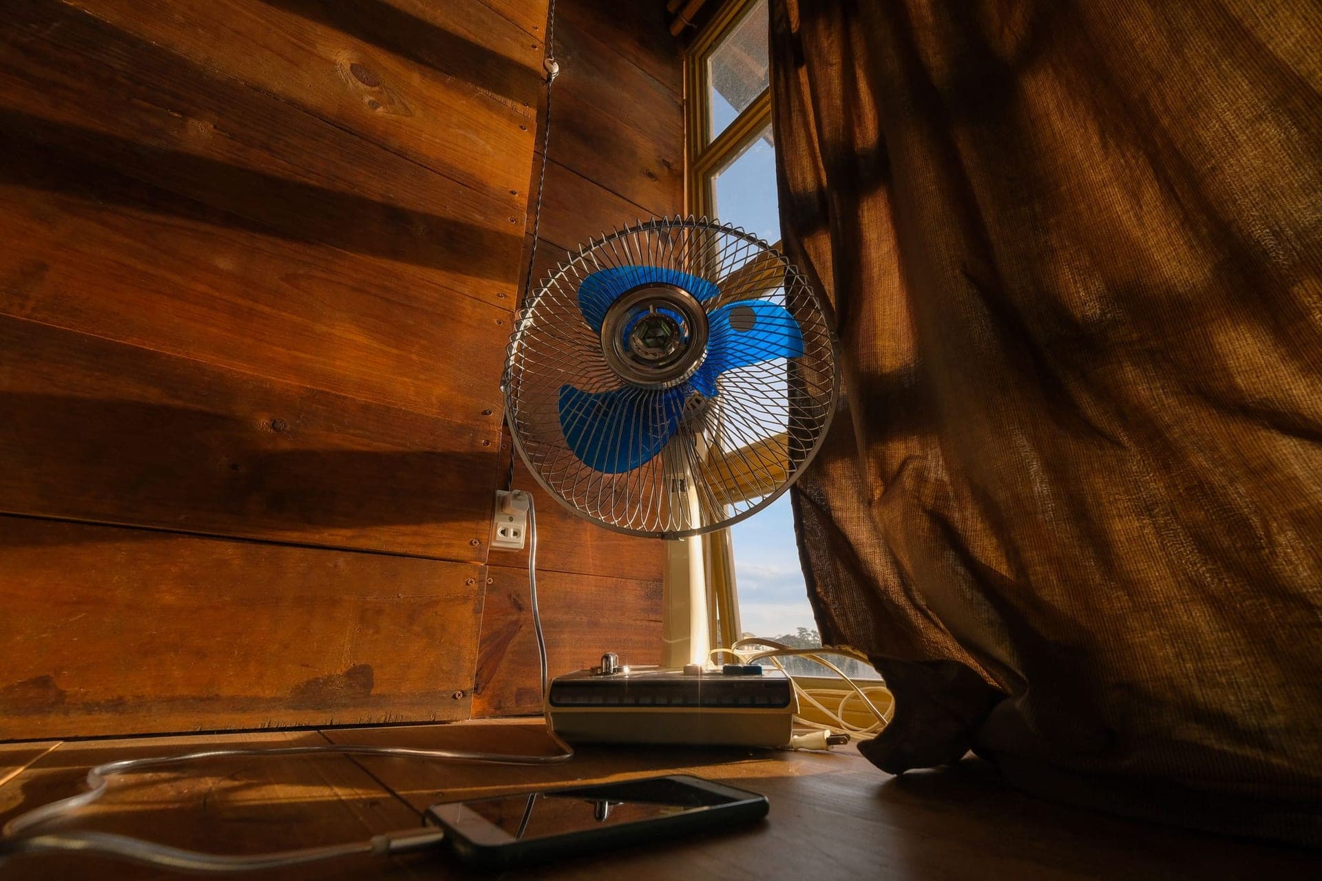 An electric fan on a table beside a sunlit window