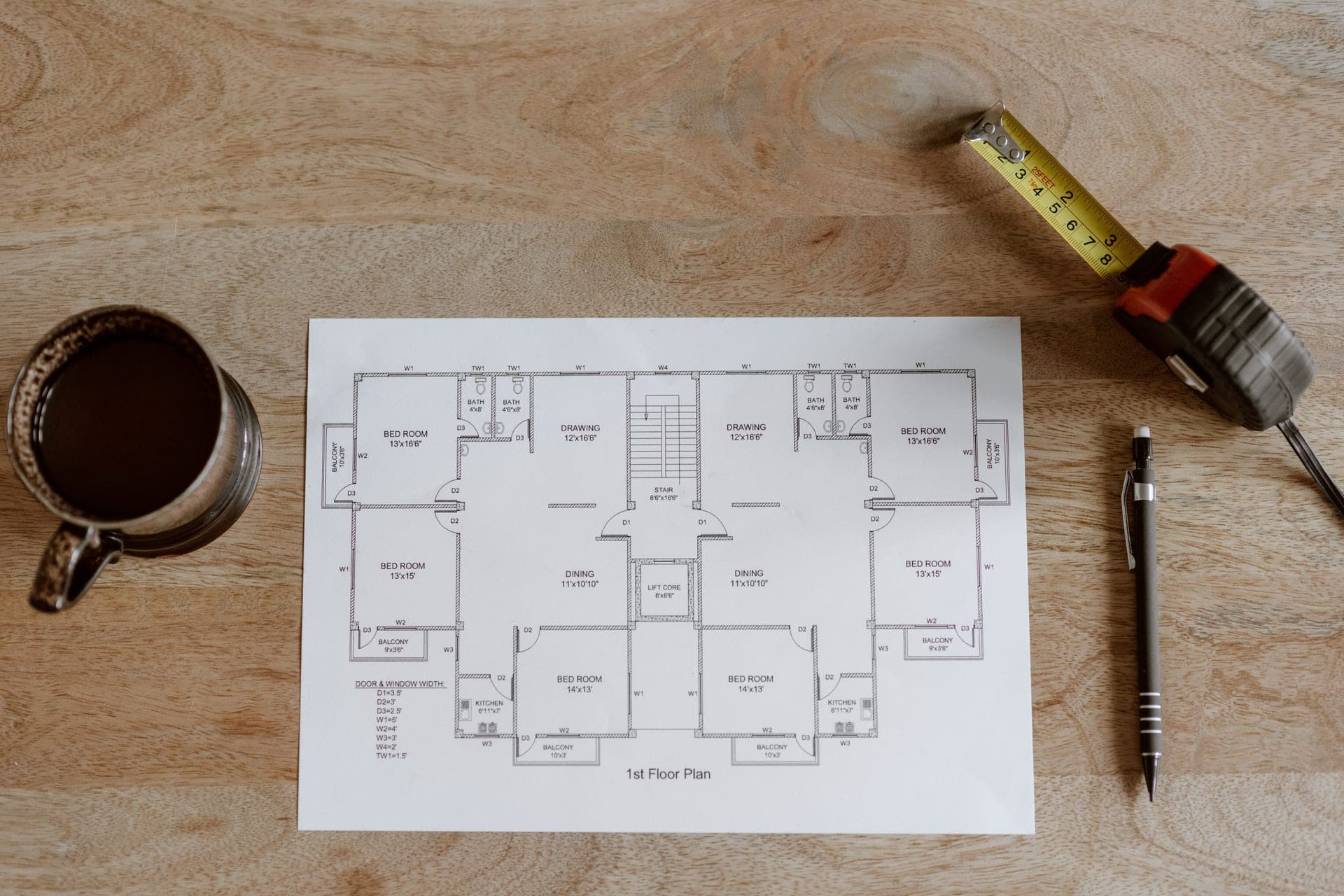 A floor plan drawing with a tape measure and pen on a wooden table