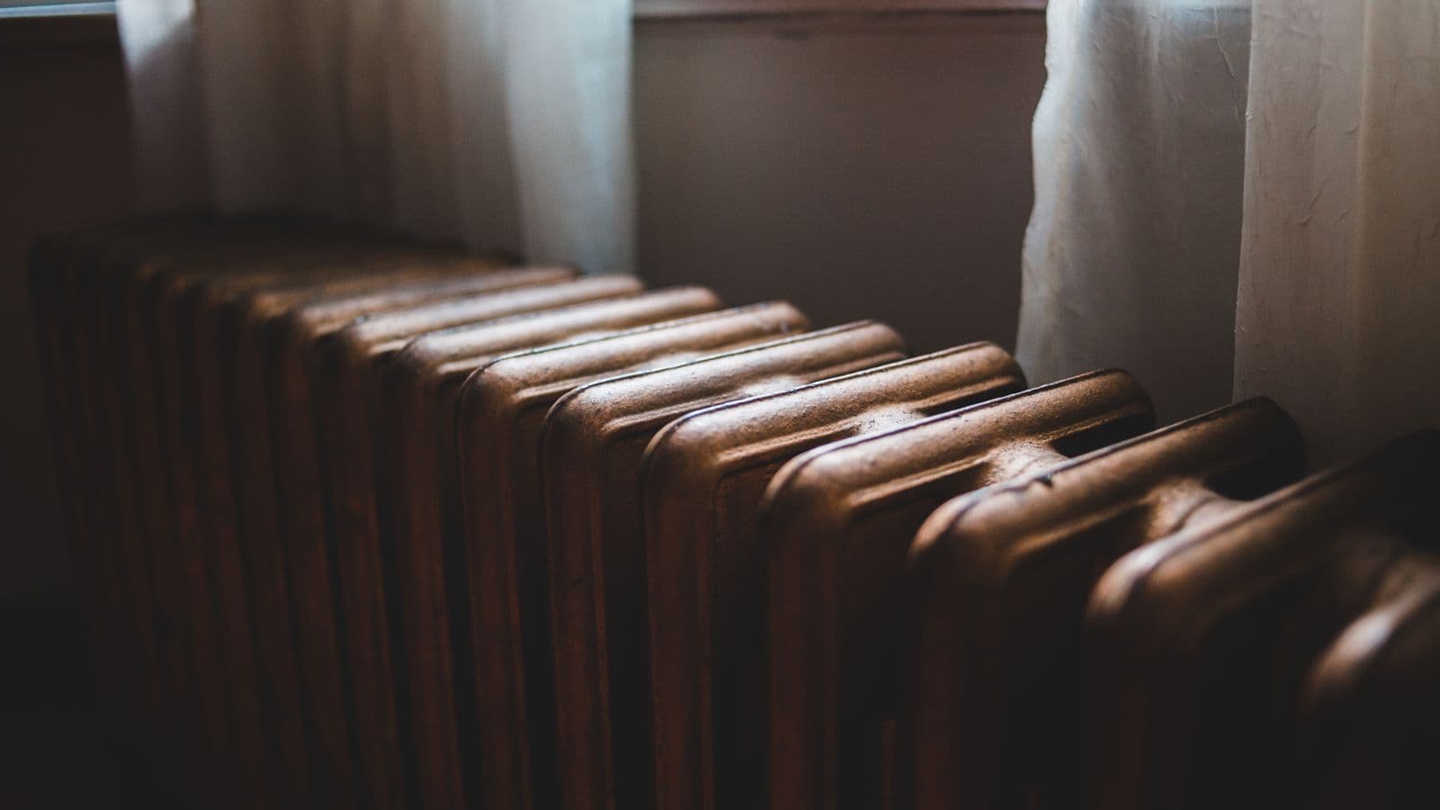 An old cast-iron radiator beneath a curtained windowsill