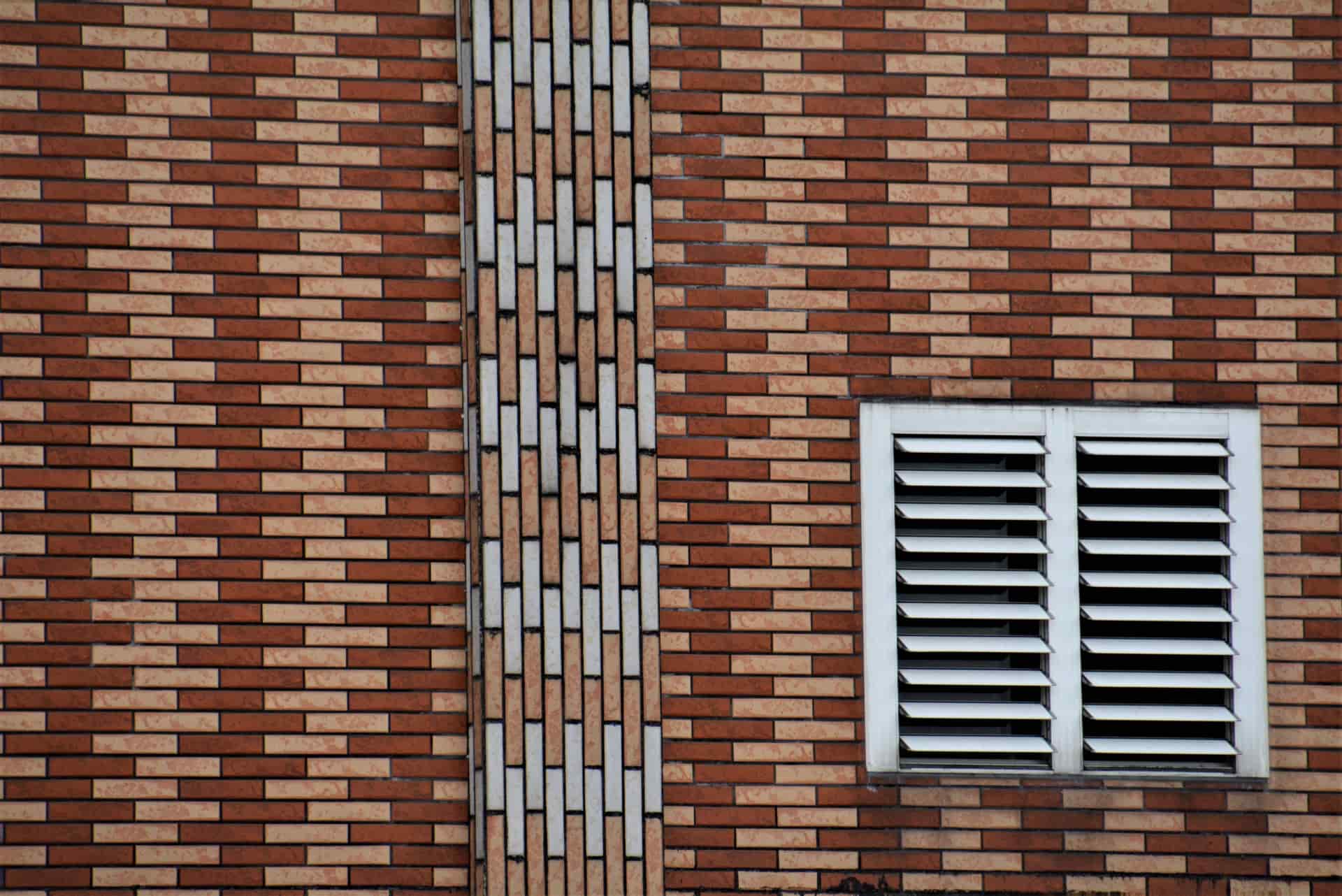 An exterior house wall with a vent grille set into the brickwork